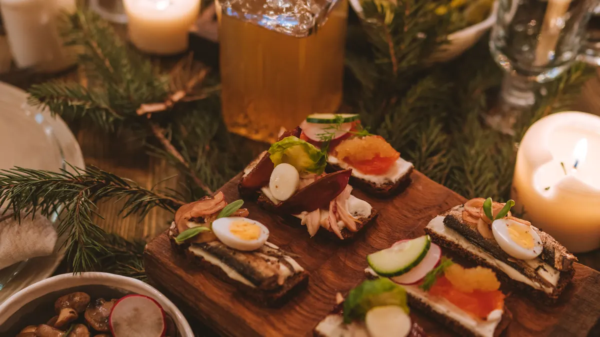 Holiday appetizer spread with candles, pine branches and a glass beverage carafe on a table
