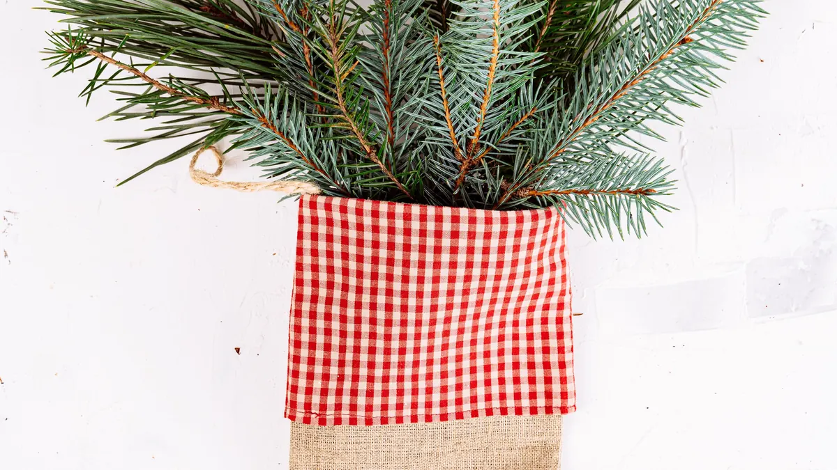 Burlap Christmas stocking filled with pine branches, hanging against a plain background